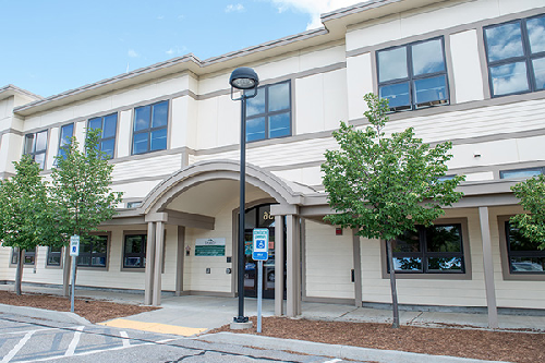 Cream colored 2-story office entrance with beige trip, windows, small trees growing in front.